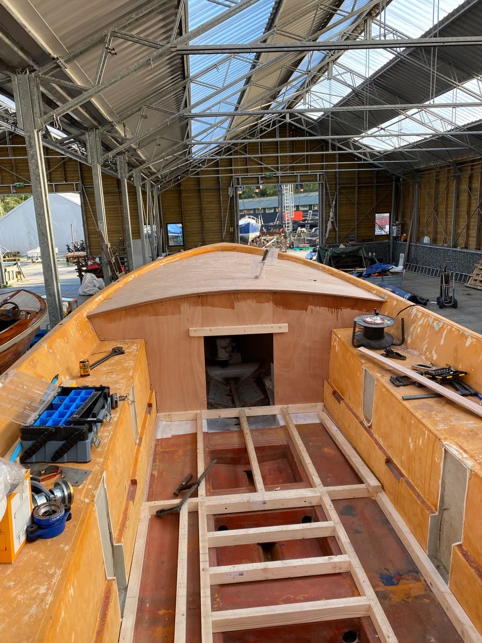 Het kale casco van de reddingsloep in de loods, met gereedschap en nieuwe spanten in de romp
