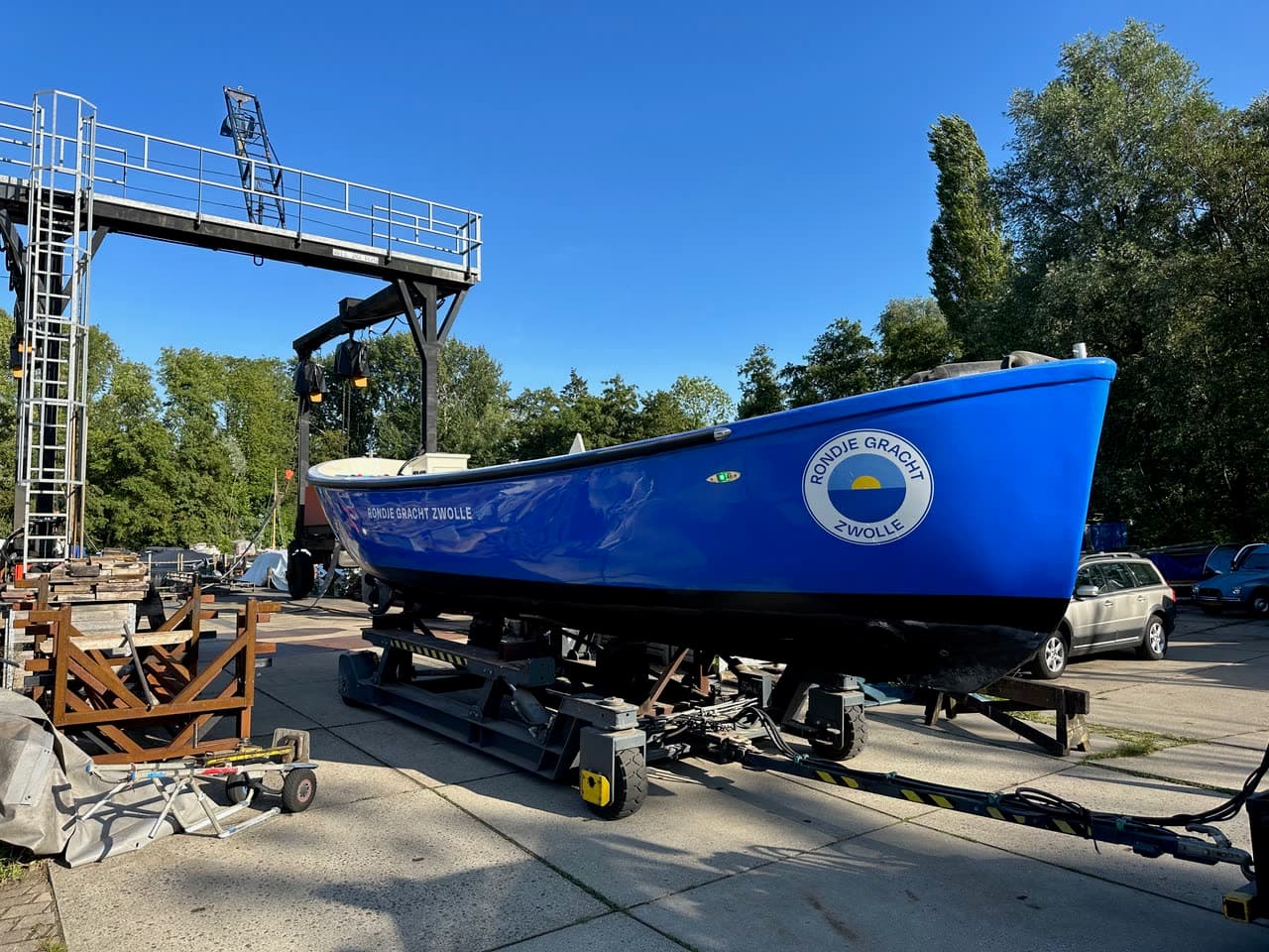 De afgebouwde blauwe sloep met logo staat op de bok bij de kraan, klaar om te water te gaan